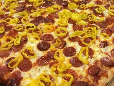 Pizza loaded with pepperoni, melted cheese, and vibrant yellow pepper rings.