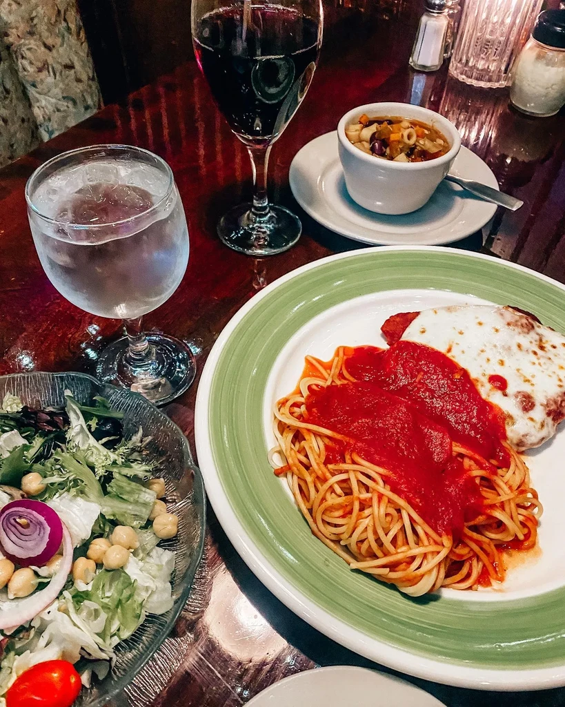 Restaurant table with spaghetti, salad, minestrone soup, and red wine.