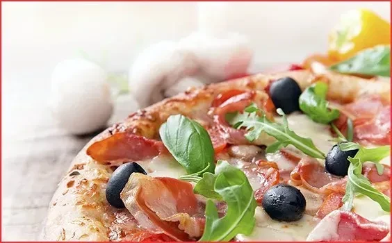 Pizza with cheese, olives, prosciutto, and arugula on wood.
