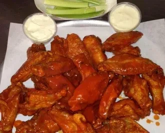 Pile of buffalo wings, creamy dipping sauce, and celery sticks.
