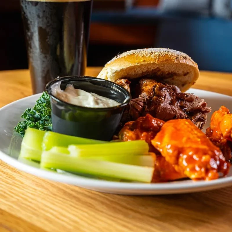 Plate of buffalo wings, pulled pork sandwich, celery, and dip.