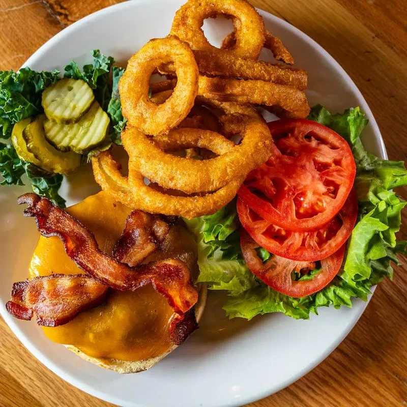 Open-faced bacon cheeseburger, onion rings, pickles, and leafy green salad.