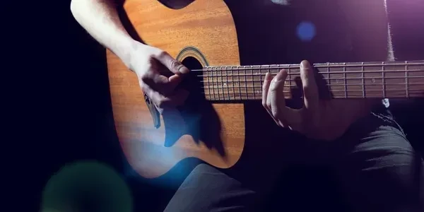 Hands strumming a wooden acoustic guitar in dim stage light.