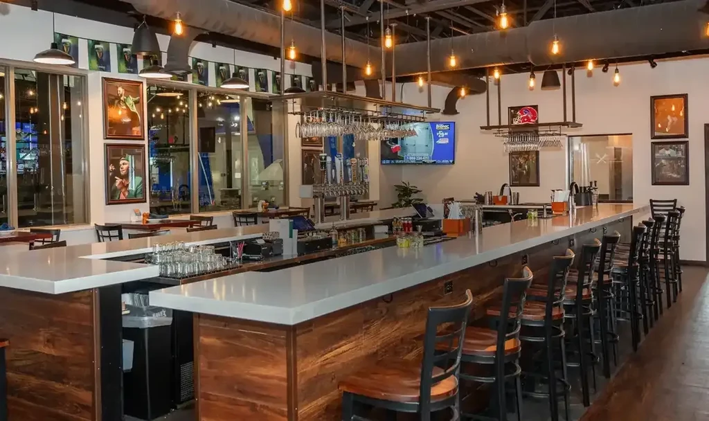 A modern, well-stocked bar interior with industrial lighting and stools.