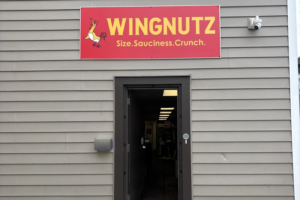 Front exterior of WINGNUTZ restaurant with red sign and open door.