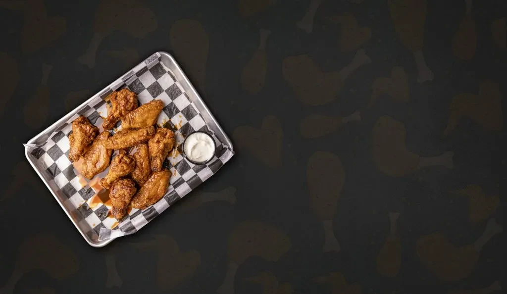 Metal tray of golden chicken wings and white dipping sauce.