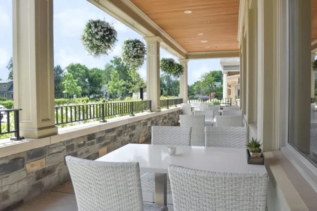 Bright outdoor dining patio with wicker chairs, stone wall, and hanging plants.