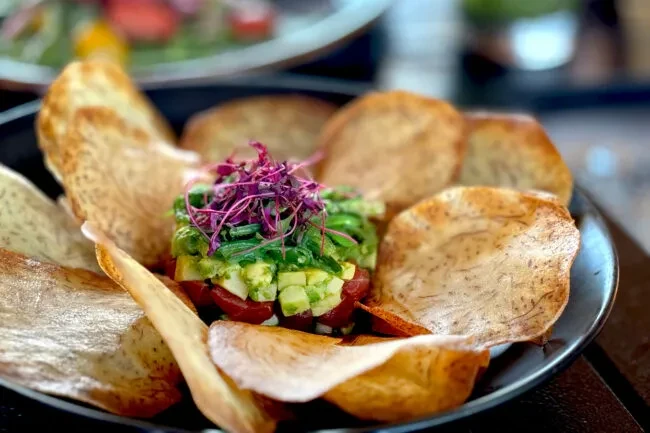 Diced green and red food with purple sprouts and root vegetable chips.