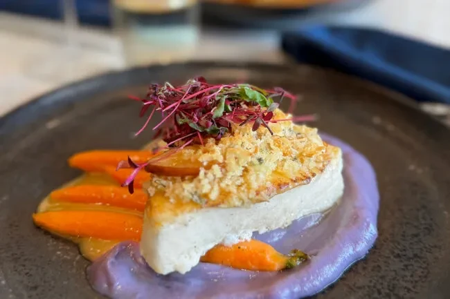 Plated gourmet protein with crispy crust, purple puree, carrots, microgreens.