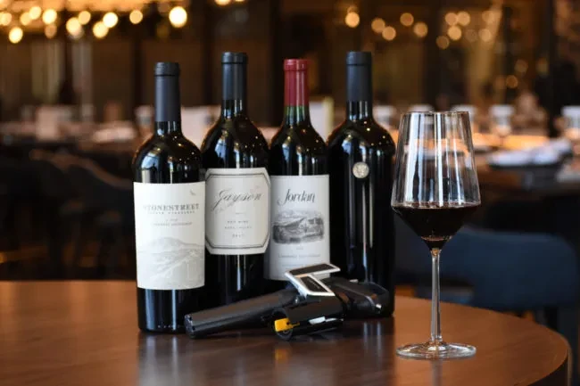Red wine bottles (Stone Street, Jayson, Jordan), glass, and opener on table.