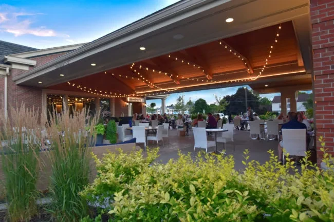 Covered outdoor restaurant patio with string lights and diners at dusk.