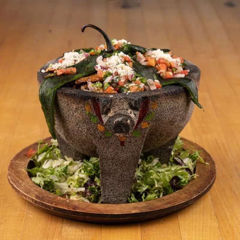 Stone molcajete filled with fresh salsa, cheese, and roasted chili peppers.