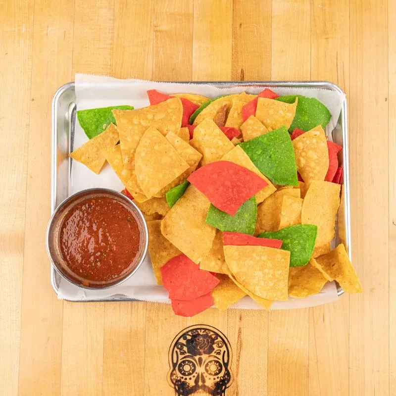 Multi-colored tortilla chips and salsa on wood with etched sugar skull.