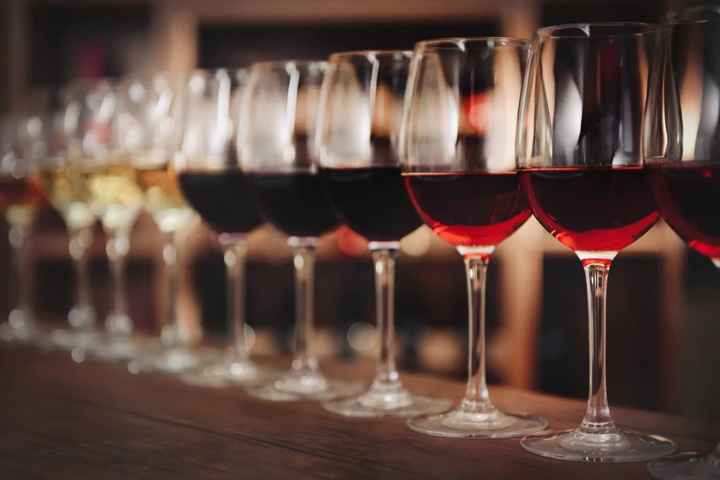 Focused row of wine glasses with various wines on dark wood.
