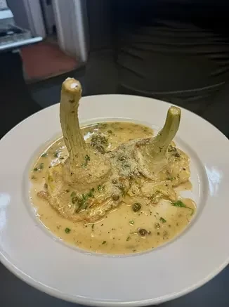 Artichokes in creamy herb and caper sauce with grated cheese on plate.