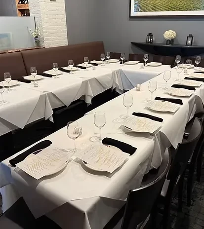U-shaped restaurant tables set with white place settings, banquette, and vineyard art.