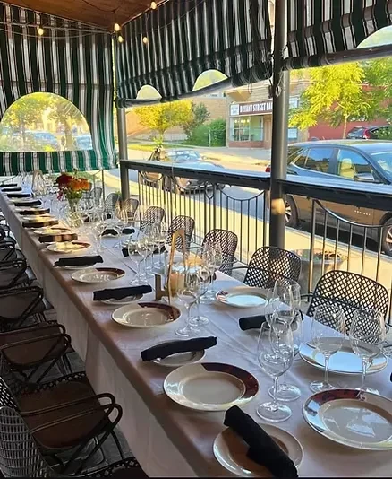 Long dining table set on a restaurant patio under striped awnings.