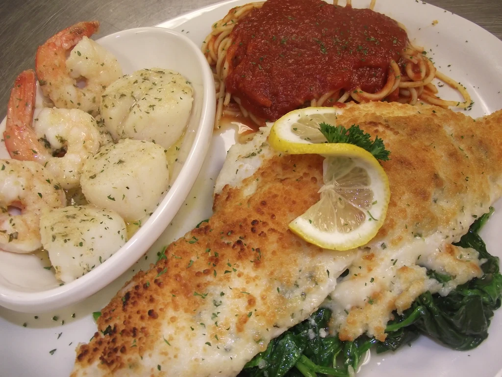 Plate of spaghetti, breaded fish over spinach, shrimp, and scallops.
