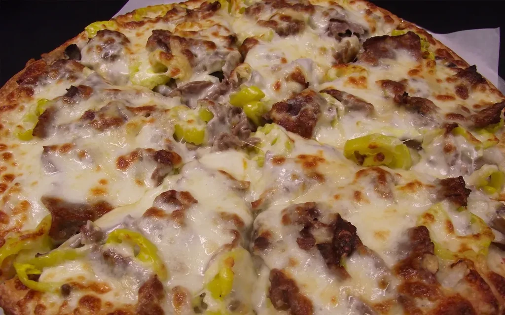Sliced pizza with melted cheese, browned sausage, and pickled peppers.