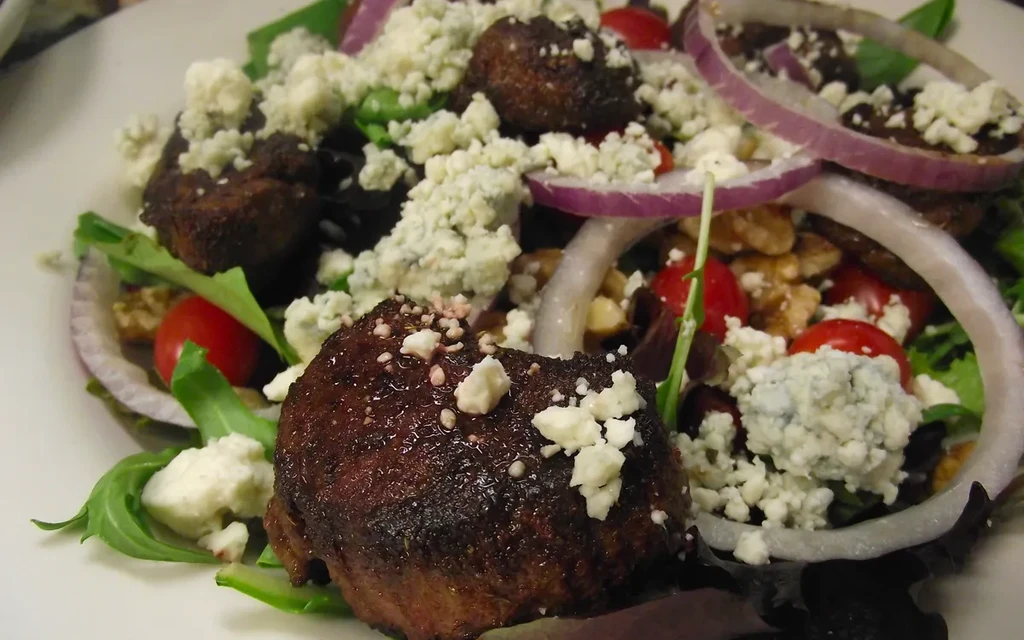 Prepared salad with seared meat, blue cheese, red onion, tomatoes, and greens.
