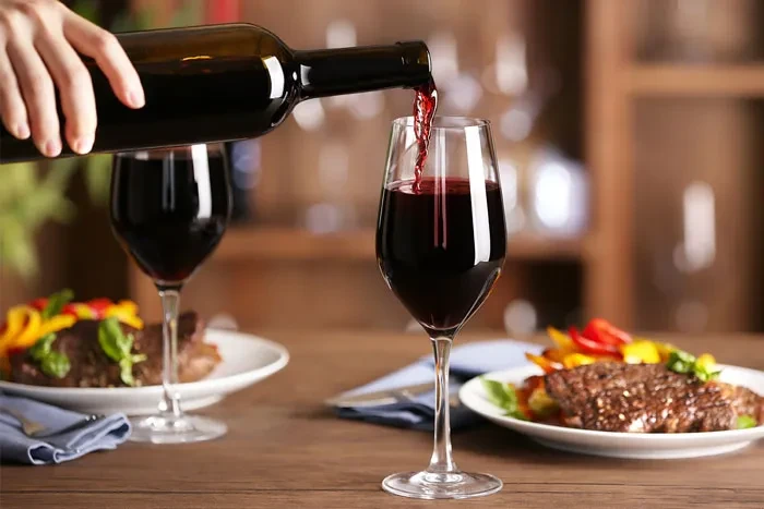 Close-up of red wine pouring into a glass beside a meal.