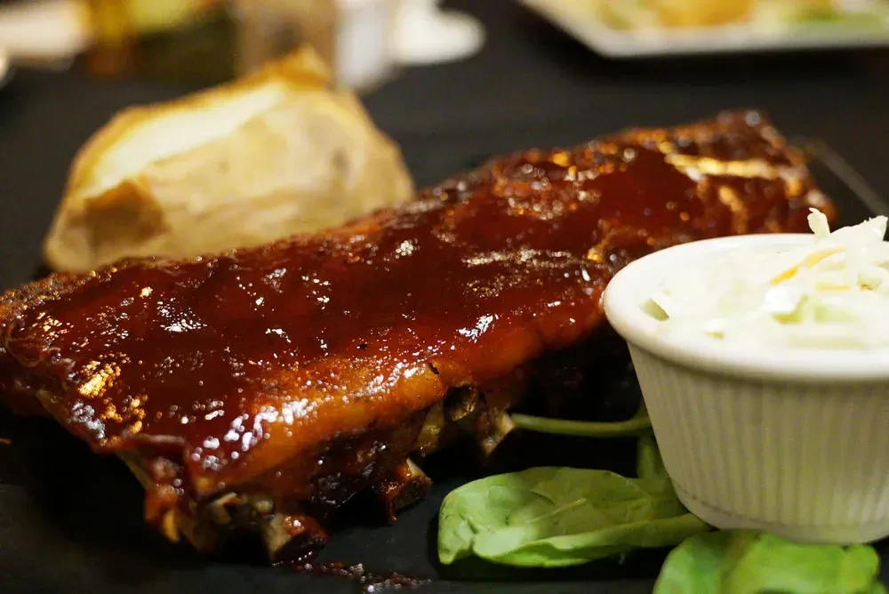 Rack of glistening barbecue ribs with baked potato and coleslaw.