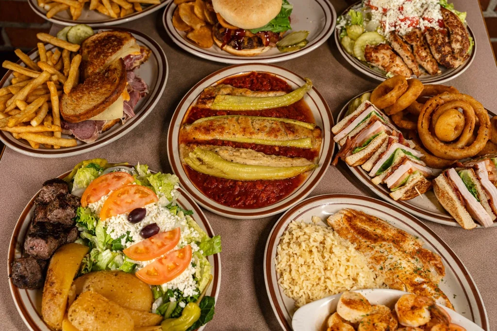 Diverse restaurant table spread with sandwiches, salads, grilled meats, and fish.