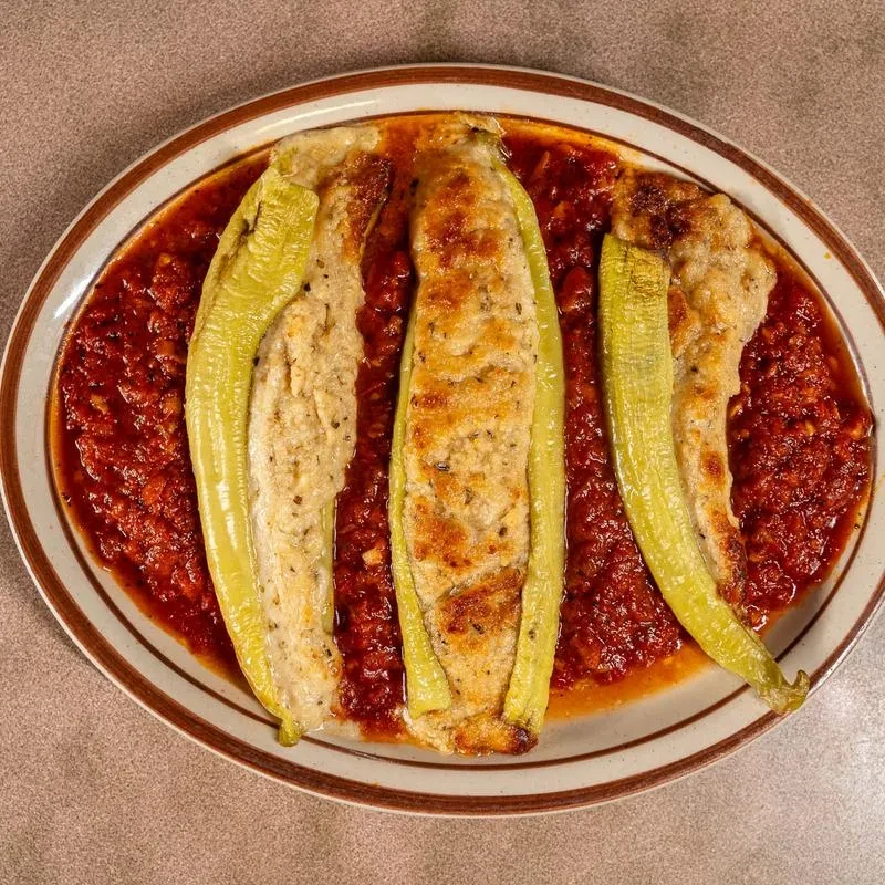 Close-up of three baked stuffed peppers in chunky red tomato sauce.