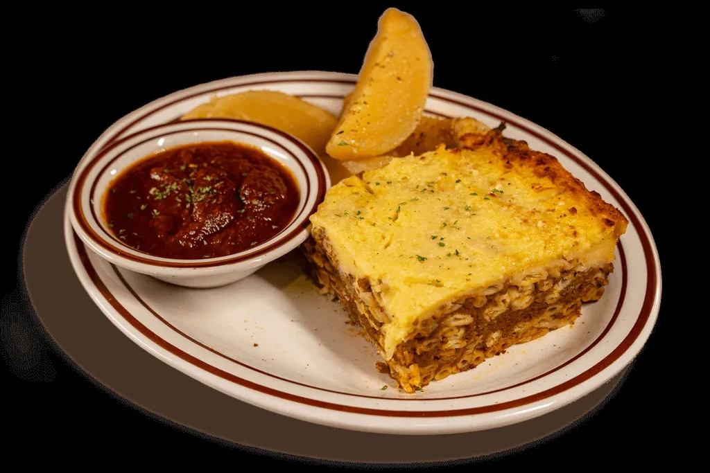 A slice of baked pasta with béchamel, side sauce, and potatoes.