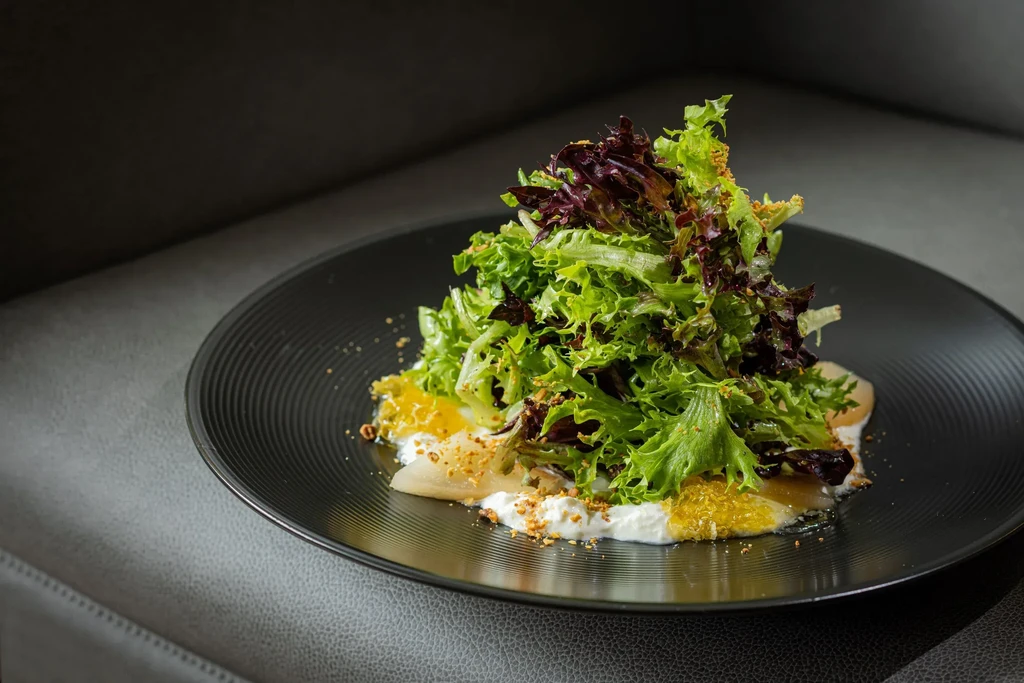A vibrant plated salad with mixed greens, fruit, creamy base, and crumbles.