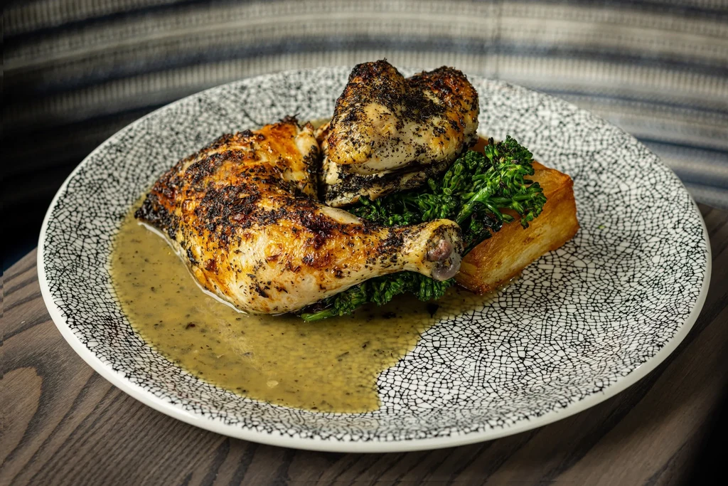 Top-down view: Roasted chicken, broccoli, potato, sauce on patterned plate.