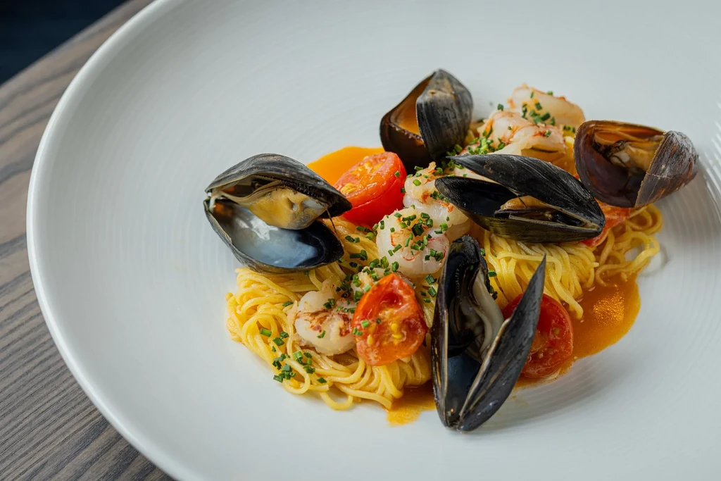 Plated seafood pasta with mussels, shrimp, tomatoes, and green herbs.
