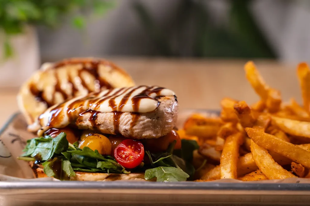 Open-faced grilled protein sandwich, fries, creamy sauce, tomatoes on a tray.
