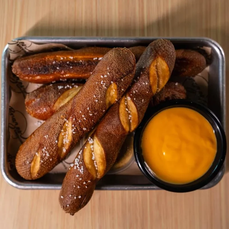 Salted pretzel sticks and orange sauce in a tray on wood.