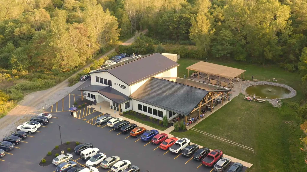 Aerial: Brazen Brewing's modern building, large outdoor dining area, pond, people.