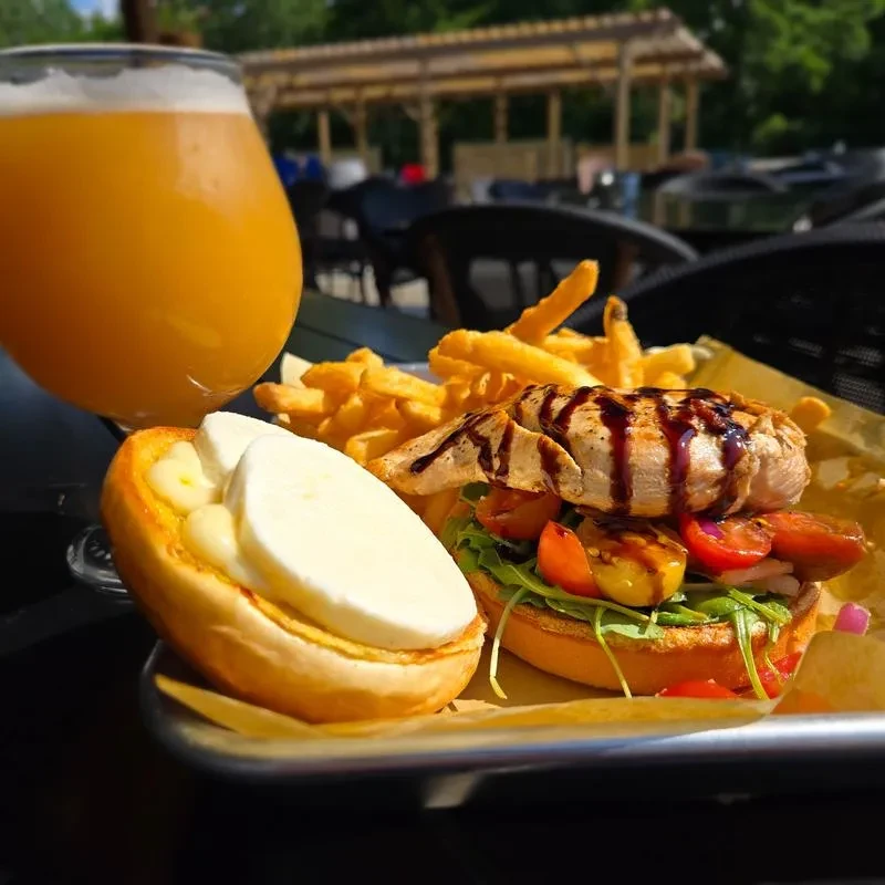 Grilled chicken sandwich, fries, and hazy amber drink served outdoors.