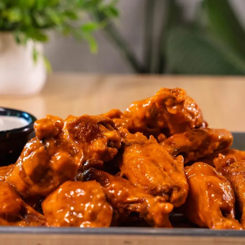 Crispy buffalo chicken wings with glossy sauce and a side of dip.