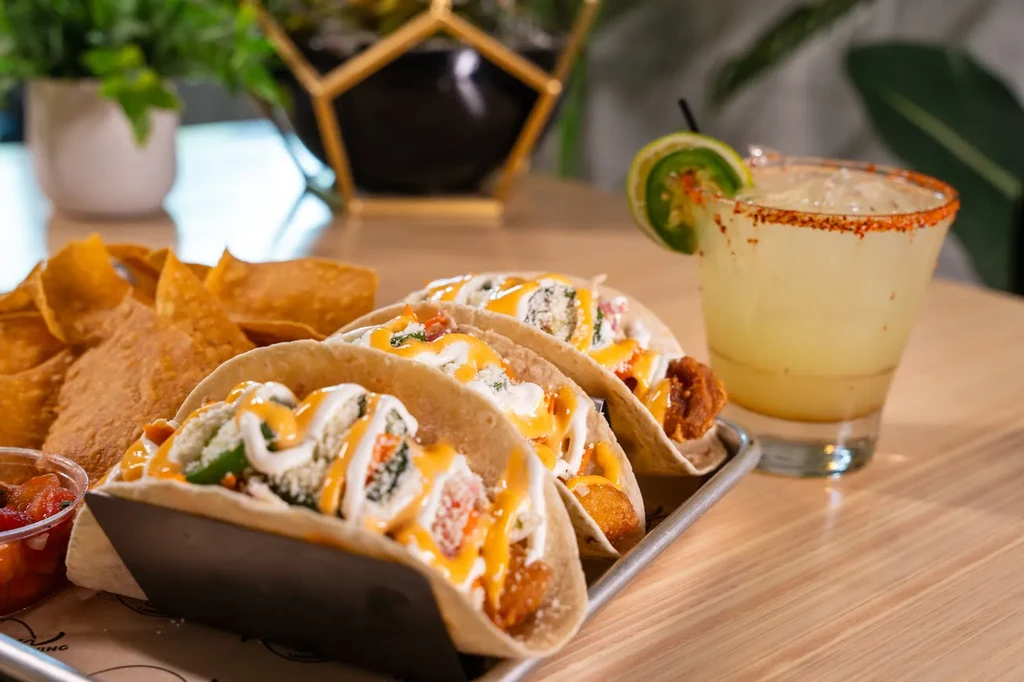 Close-up of three tacos, chips, salsa, and a margarita cocktail.