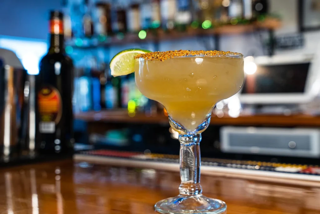 Spiced margarita with lime wedge on a dimly lit wooden bar.