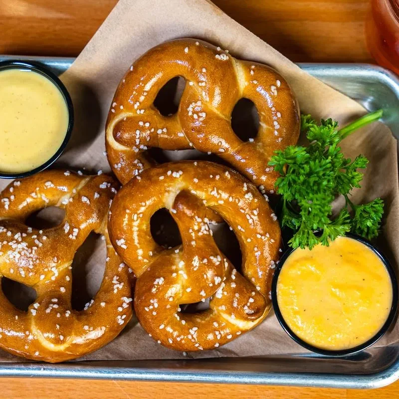 Three golden-brown salted pretzels, two dipping sauces, and parsley garnish.
