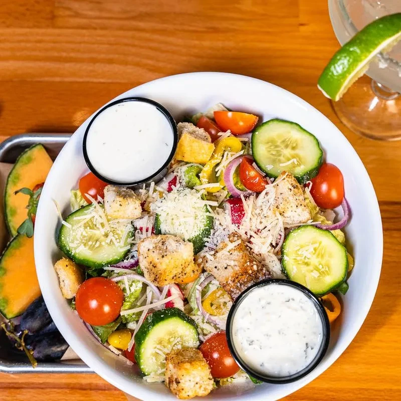 A chicken and vegetable salad with Parmesan, fruit, drink on wood.