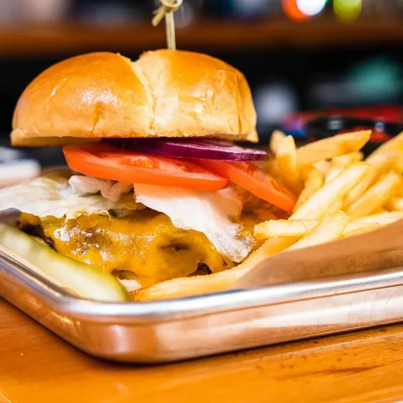 Gourmet burger with fried egg, crispy fries, and pickle on silver tray.