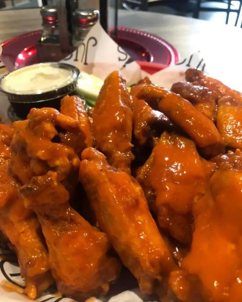 Close-up: basket of buffalo chicken wings, creamy dip, and celery.