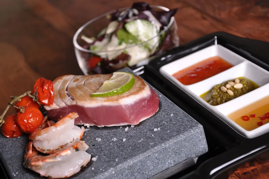 Seared tuna, shrimp, roasted tomatoes, and three sauces on a stone.