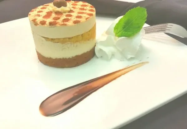 Cylindrical layered dessert with whipped cream, mint, and dark sauce.