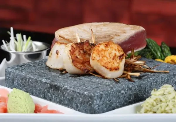 Seared scallops, raw tuna, and garnishes professionally plated on a stone slab.