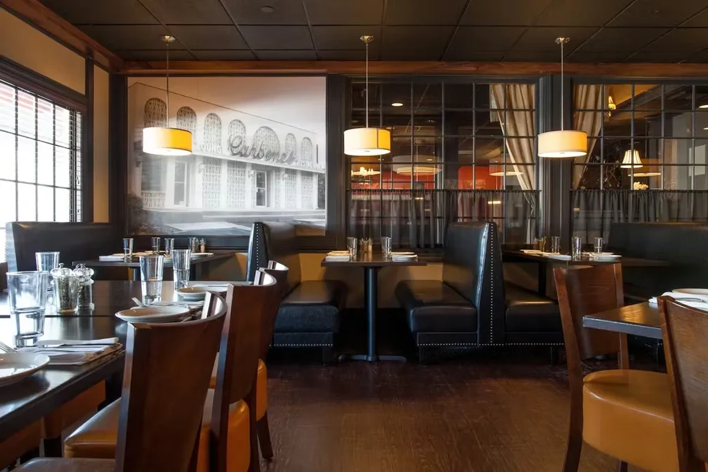 Elegant restaurant interior with set tables, booths, and "Carbone's" mural.