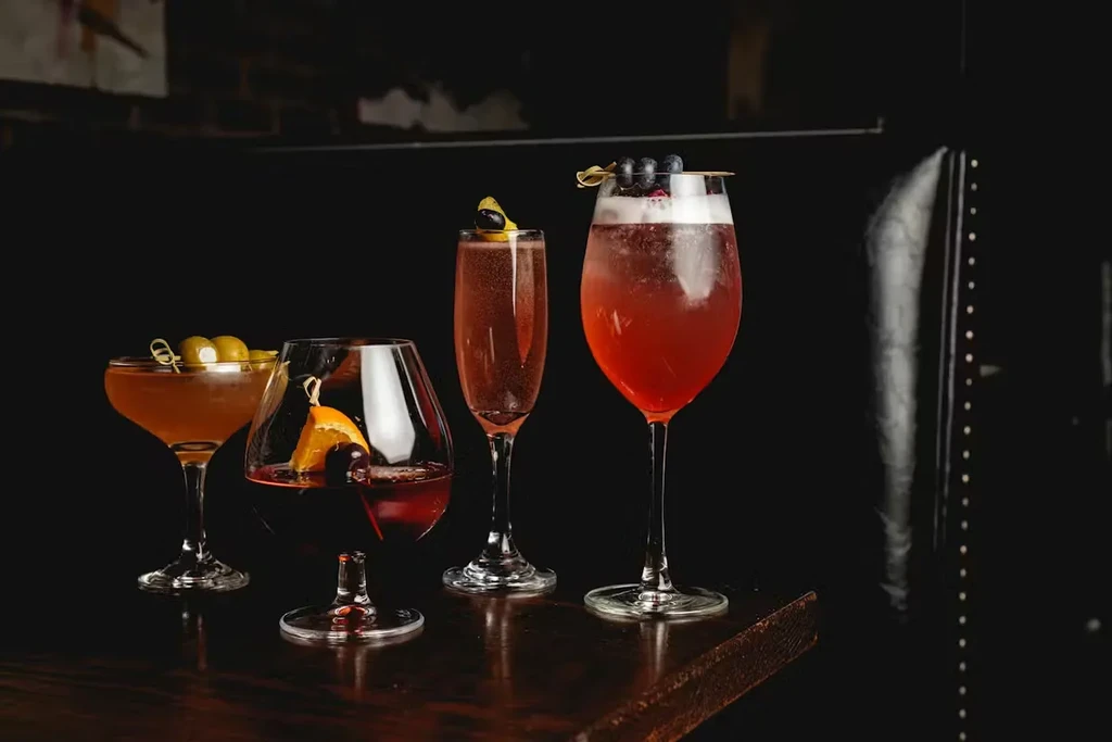 Four distinct cocktails with various garnishes on a dark bar.