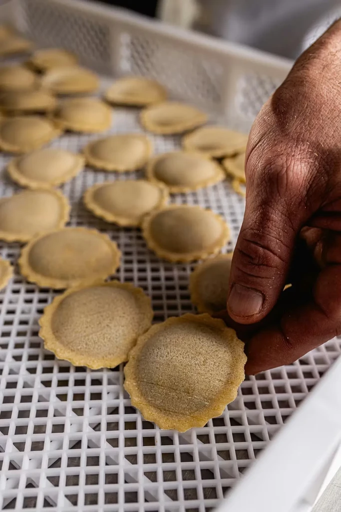 Hand holds unbaked, crimped pasta pieces on a drying tray.