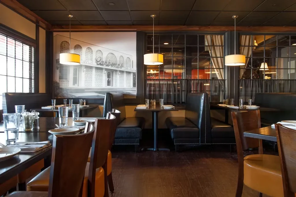 Dark, upscale restaurant dining room with set tables and a 'Carbone's' mural.